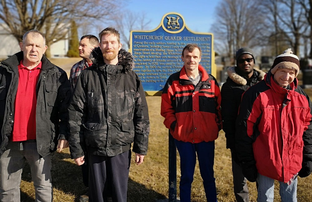 group of male residents in front of a Quaker Settlement sign