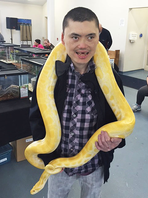 Man holding a yellow snake wrapped around his shoulders